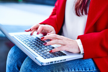 Young woman's hands with red nails tipping while works using her computer on a cloudy winter day....