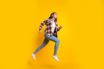 Fototapeta na wymiar Full length photo of shiny pretty lady wear checkered shirt jumping high hurrying empty space isolated yellow color background