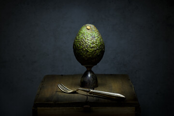 Single whole avocado and fork on a wooden box fine art still life.