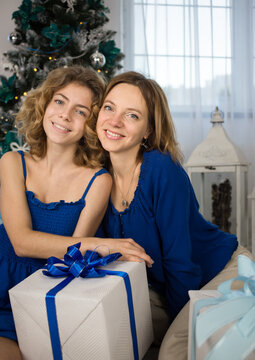 portrait of two happy women, mom and her adult daughter near the festive Christmas tree with a big gift box. The magic of New Year's Eve. The concept of a friendly family celebration of Christmas