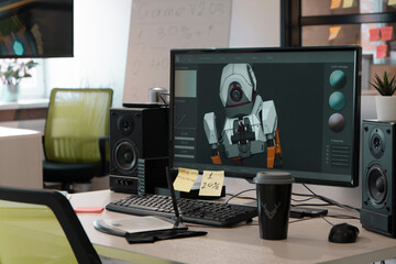 Designer's computer on a table with a 3D model of a dog robot on a monitor screen in a game and application development studio