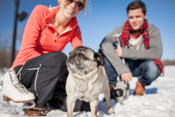 Couple kneeling in the snow with pet pug dog.