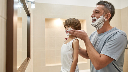 Side of father smear shaving foam on son face
