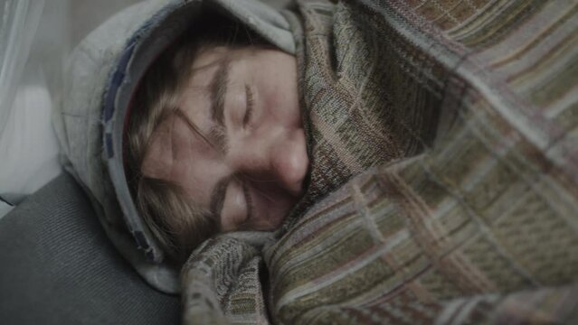 Close up shot of homeless man pulling blanket over face and sleeping on ground on cold day