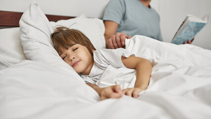 Father covering sleeping son with blanket in bed