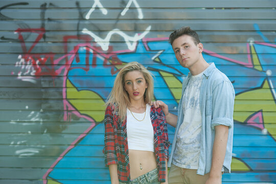 Teenage girl and boy standing in front of graffiti on wall.