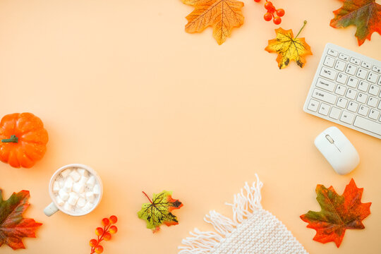 Autumn office workspace. Autumn flat lay background. Keyboard, laptop with autumn cloth and fall decorations - pumpkin, leaves and other.