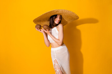 Photo of sweet dreamy lady wear white outfit hat holding two coconuts smiling isolated yellow color background