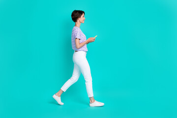Fototapeta na wymiar Full length photo of sweet shiny girl dressed purple t-shirt walking empty space chatting modern device isolated teal color background