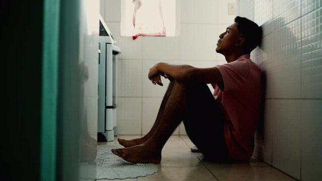Anxious young South American man sitting on floor feeling worried emotion. Stressed person feeling overwhelmed by modern problems. Lonely Brazilian guy