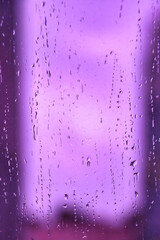 Naklejka na ściany i meble Abstract purple backgrounds with raindrops on blurred daylight. Rain drops on window glass for background rainy fall autumn weather. Outside urban window is blurred bokeh water. Copy text space