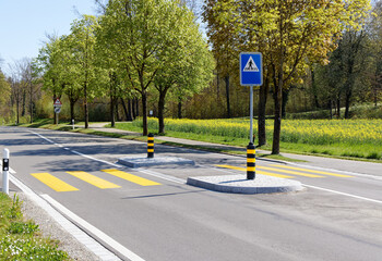 pedestrian crossing with island, blue pedestrian sign in nice spring weather, green trees in the background, school start watch out for children who want to cross the street
