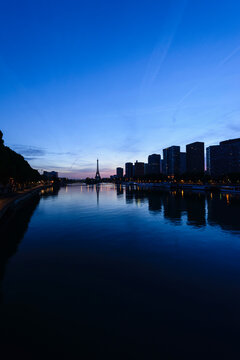 A view along the water of the River Seine at night, tall buildings on the river bank, the Eiffel tower in the distance.