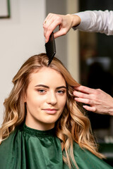 Hairdresser combing long hair of young caucasian woman looking at the camera and smiling in beauty salon