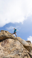 low view of man walking on a rock cliff with blue sky in background . copy space
