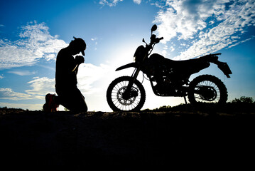 Silhouette of a lonely, heartbroken, disappointed man having a motocross bike on the mountain in a...