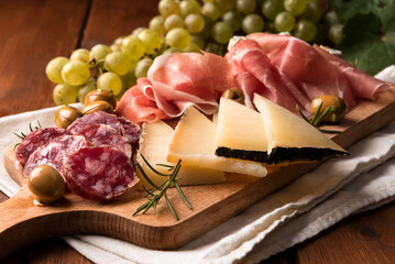 Tagliere con tipici salumi, prosciutti, olive, uva fresca e formaggi - cibo italiano 