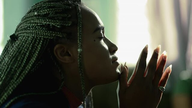 Faithful African American young woman praying to God. Hopeful South american latina Brazilian adult girl in prayer at home
