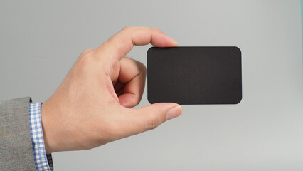 Hand is holding black empty card and wear suit on gray background. business man