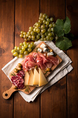 Tagliere con tipici salumi, prosciutti, olive, uva fresca e formaggi - cibo italiano 