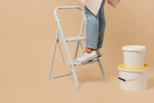 Cropped close up employee laborer handyman woman feet in jeans stand on ladder use wall paint bucket isolated on plain beige background Instruments accessories for renovation room Repair home concept.