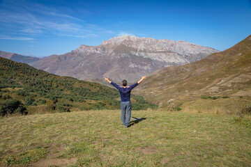 An adult man stands on top of a mountain with outstretched arms.