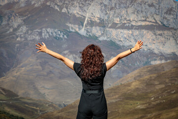 A young woman stands on top of a mountain with her arms outstretched.