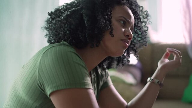 A pensive black woman playing with curly hair at home. African American girl plays with hair