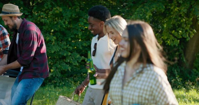 Friends arrive for an open-air camper trip to the lake together. They organize a picnic spread out deck chairs poufs for relaxing and barbecuing.