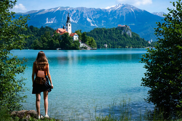 beautiful woman in a short skirt stands on the shore of lake bled in slovenia with a view of the...