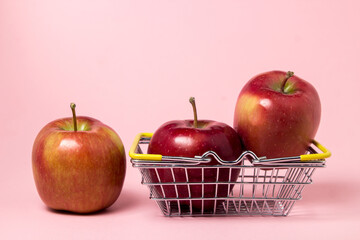 Red apples on a pink background. Small shopping basket full of apples