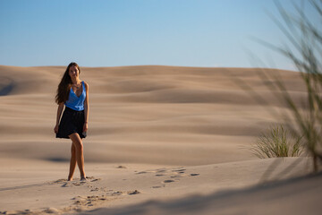 young long-haired woman with huge dunes and sandy hills in the background; woman lost in the desert