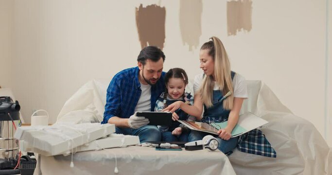 A cute blonde woman, together with family, is shopping online for new apartment, which is under renovation. The happiest is the little girl who was bought a new bed in renovated children's room.