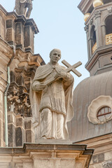 Fototapeta premium Old roof statute of priest or monk holding a big cross at Dome base of the Cathedral of Holy Trinity, historical center of Dresden, Germany.
