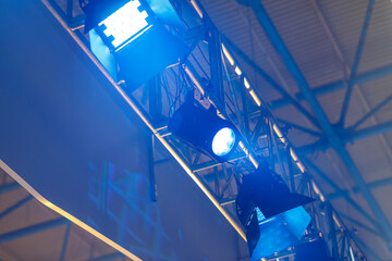 Professional lighting fixtures are suspended on a pole above the stage, they shine with yellow cold...