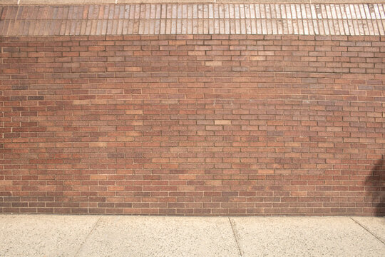 red brick wall with finishing top bricks and concert sidewalk walkway path