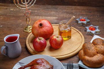 for Rosh Hashanah near pomegranate honey apples wine and challah on a wooden table and candles.