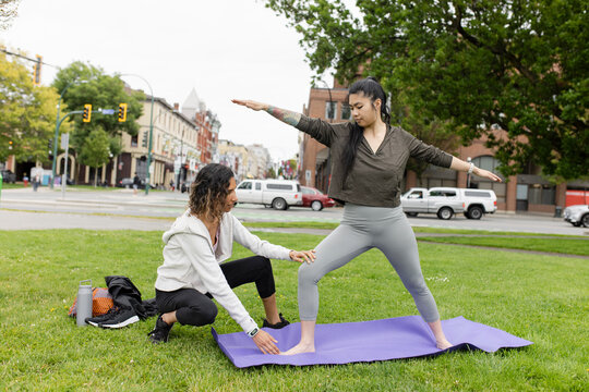 Instructor guiding woman practicing yoga in urban park