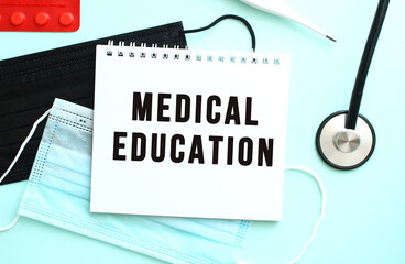 The text MEDICAL EDUCATION is written in a notebook that lies on a blue background next to a medical masks