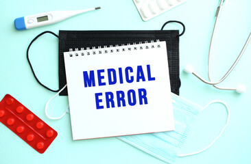 The text MEDICAL ERROR is written in a notebook that lies on a blue background next to a thermometer and medical masks.