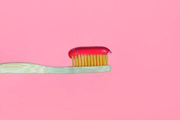 Wooden bamboo toothbrush with toothpaste on a pink background.