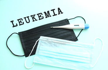 LEUKEMIA lettering on a blue background with blue and black medical masks lying next to it.