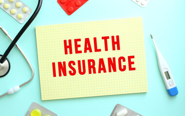 The text HEALTH INSURANCE is written in a yellow notebook that lies next to the stethoscope,...