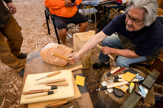 Male Indigenous artist with knifes carving wood in workshop