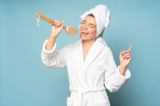 Woman singer taking high note singing in massage brush on blue background dressed in bathrobe
