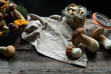 Glass jar with dried porcini and fresh porcini on wooden table on dark background 