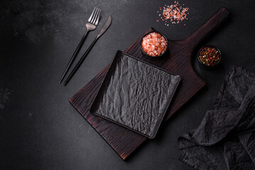 Fototapeta premium Empty black plate over dark stone background with free space. Top view