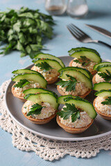 Tartlets with cod liver, egg, garnished with cucumber and parsley on plate on blue background