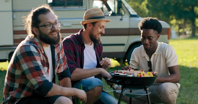 A bearded middle-aged guy is preparing a barbecue for friends. A group of college boys hang out together. RV trip.