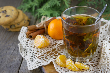 Christmas (New Year) composition. Glass cup of tea with mint, tangerine slices, cinnamon sticks, chocolate chip cookies and thuja branches on wooden background